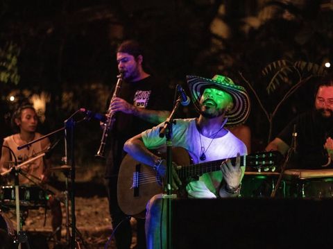 A live band playing outdoors at night, a singer with a guitar in front