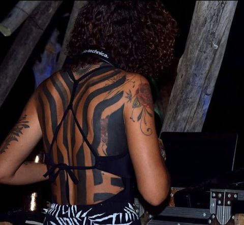 A DJ seen from behind at the decks, under a wooden structure